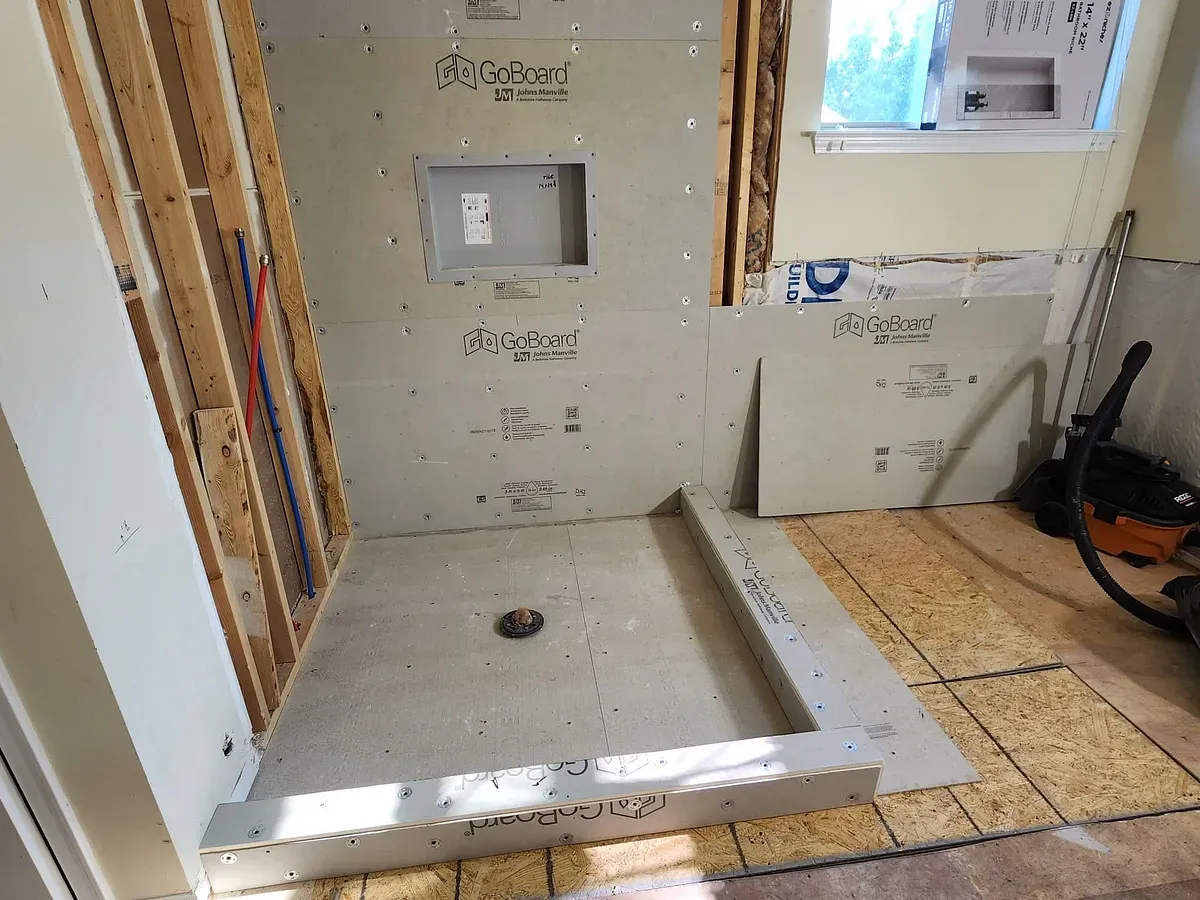 A shower alcove built out with waterproof tile backer board and a sloped pan, ready for tile.