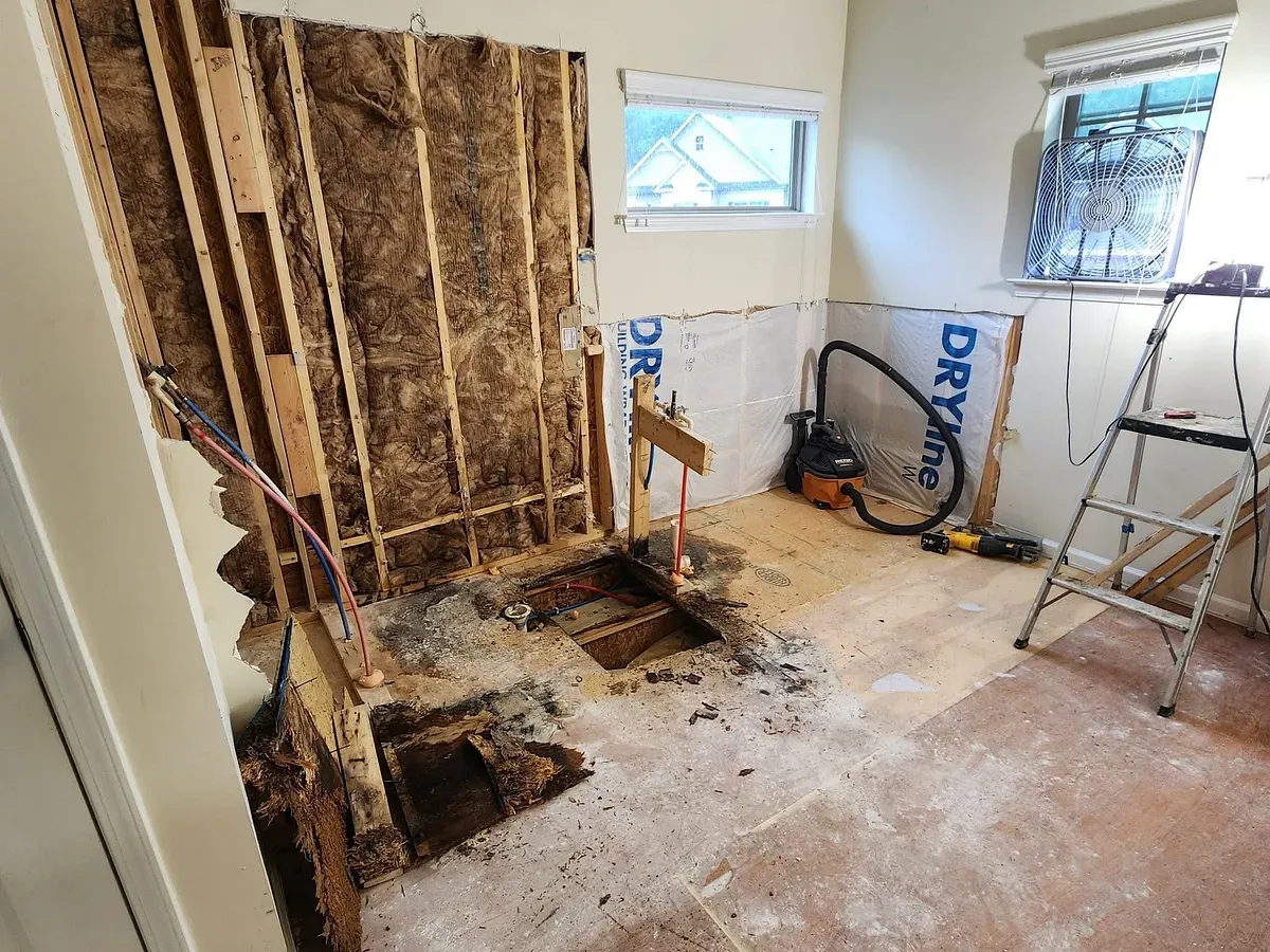 A bathroom stripped to the studs during demolition, exposing water-damaged framing and a torn-out subfloor.